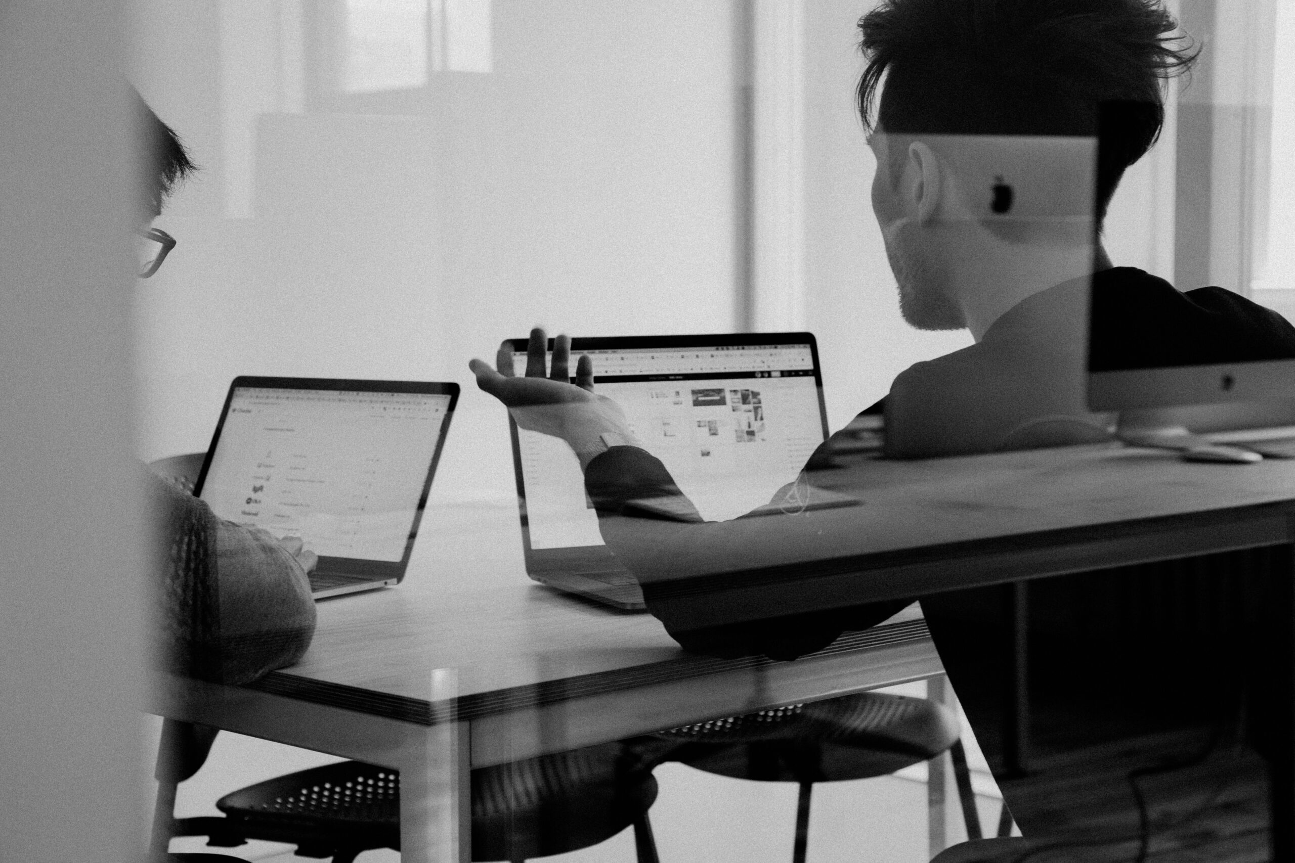 Zwei Personen sitzen in einem Büro vor ihren Laptops.