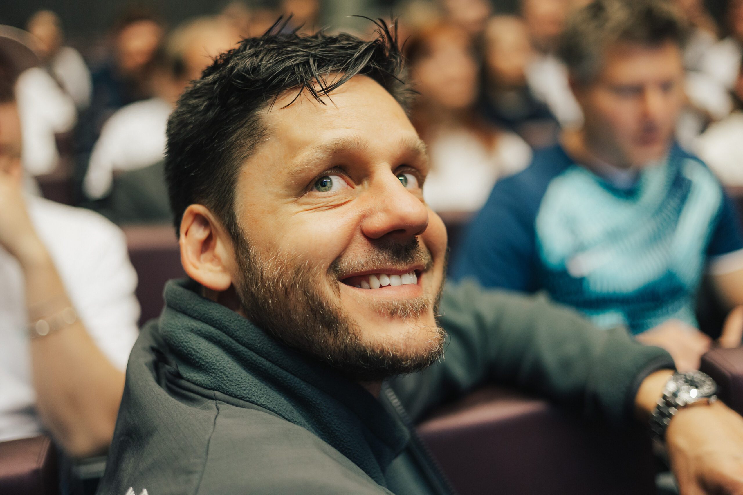 Ein Mann sitzt in einem Meetingraum und lacht mit dem Gesicht zur Kamera gedreht
